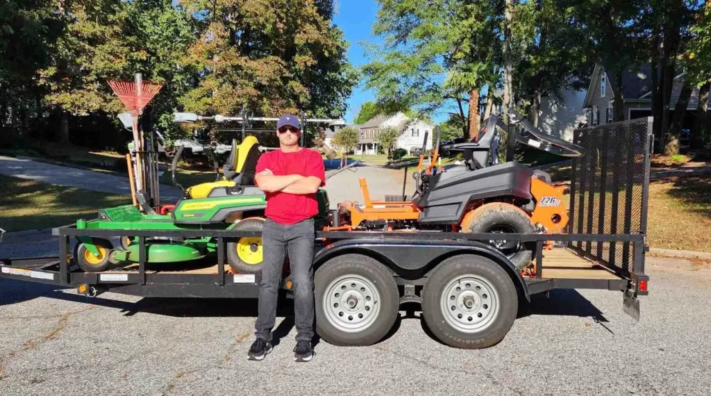Jason Yard Scaping worker standing by a trailer loaded with mowers and lawn equipment in Greenville, SC.